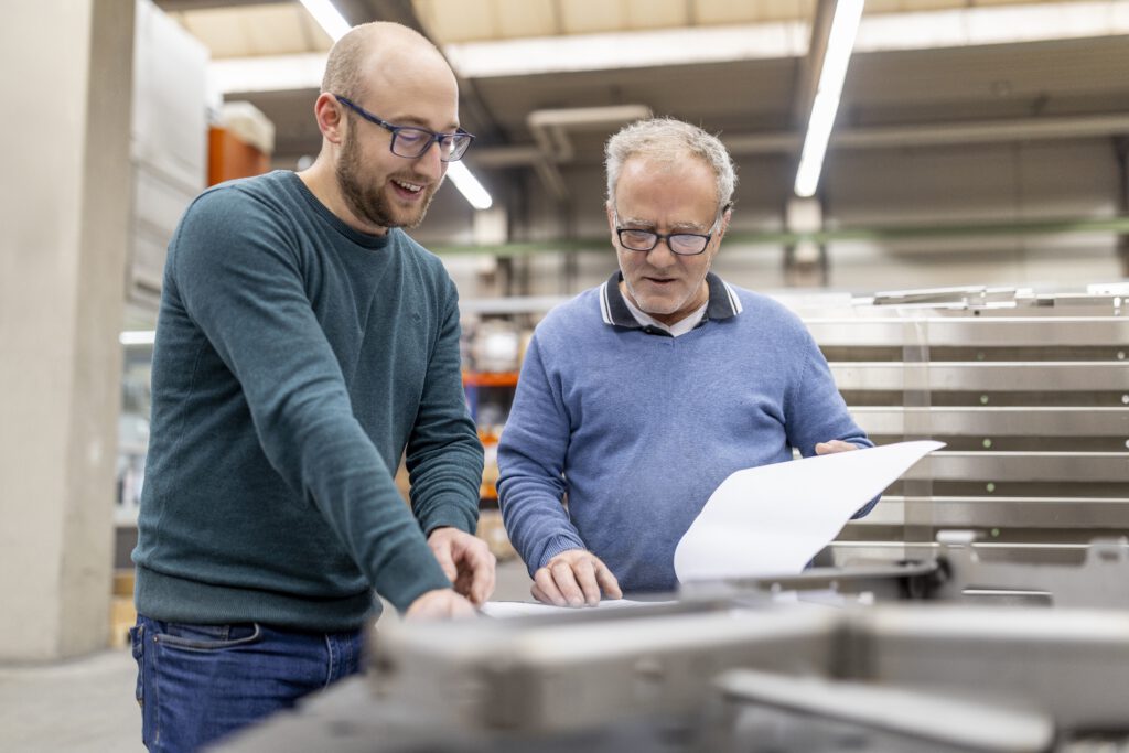 Zwei Maenner In Einer Werkstatt Besprechen Plaene Fuer Metallverarbeitung.