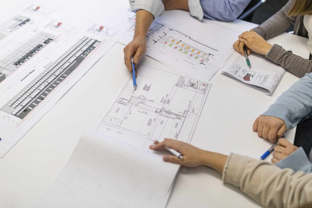 Personen bei einer Besprechung ueber Architekturentwuerfe am Tisch