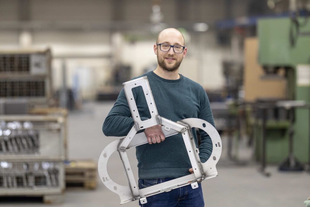 Ein Mann haelt einen Metallrahmen in einer Fabrikumgebung.