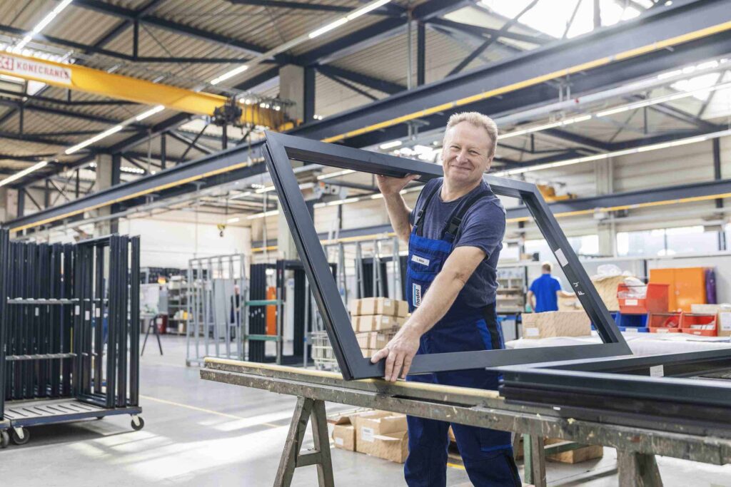 Ein Arbeiter in einer Industriehalle montiert Fensterrahmen.