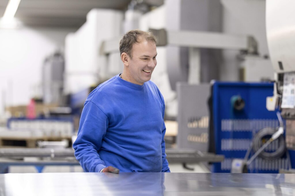 Person in blauer Arbeitskleidung in einer Fabrikhalle neben Maschinen