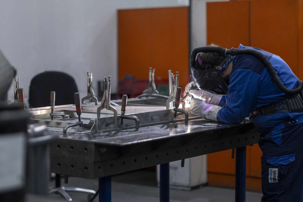 Person in Schutzkleidung arbeitet an einem Metallstueck in einem Labor.