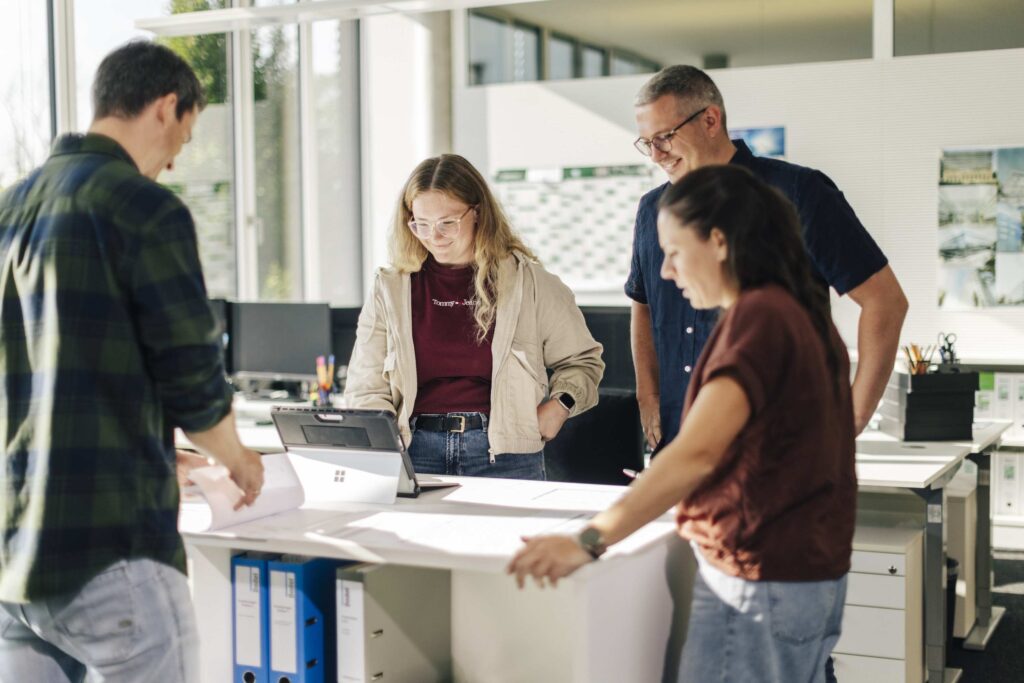Ein Team von vier Personen bespricht ein Projekt an einem Tisch im Buero.